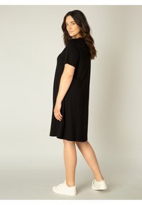 Zwart korte mouwen jurk met een ontspannen pasvorm en een knielange zoom, gemaakt van zacht materiaal, gecombineerd met witte sneakers.