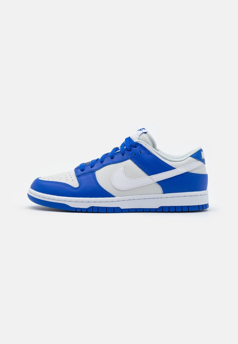 Baskets basses avec une base en cuir blanc et des superpositions bleues, lacets bleus, logo Nike blanc et semelle bleue, vues de profil.