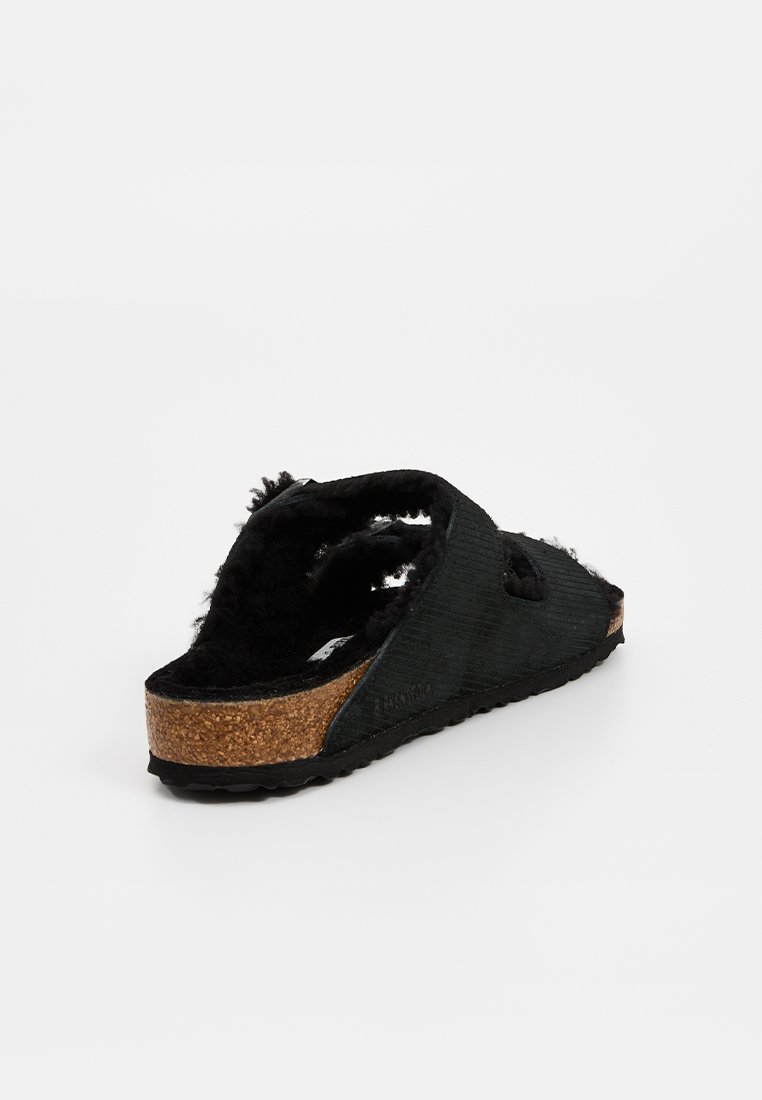 Sandale noire à enfiler avec un dessus en tissu texturé, une semelle intermédiaire en liège et une doublure intérieure douce pour le confort. Design ouvert avec découpes latérales.