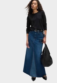 Gonna maxi in denim con vita alta e design svasato, abbinata a un maglione nero a maniche lunghe e a una borsa nera testurizzata.