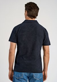 Marine polo shirt met een zachte textuur, korte mouwen en een kraag, in combinatie met lichtblauwe denim jeans. Eenvoudig en casual ontwerp.