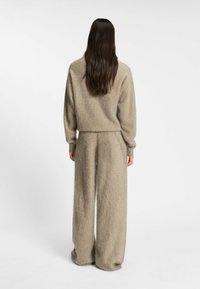 Beige, fluffig stickad tröja och matchande vida byxor, tillverkade av mjukt material. Designen har en avslappnad passform med ribbade detaljer vid ärmsluten.