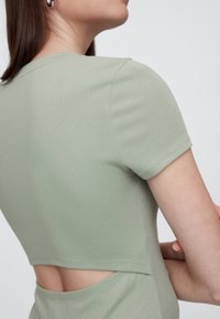 Zielony krótki top z teksturowanym wykończeniem i wycięciem na plecach, z okrągłym dekoltem i dopasowanym krojem.