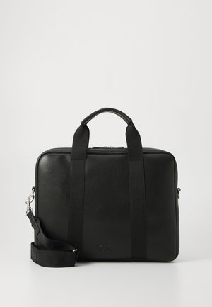 Malette en cuir noir avec des poignées en tissu et une bandoulière réglable. Présente une surface texturée et un logo à l'avant.