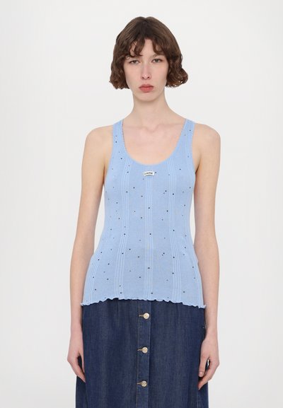 Lys blå ribbede tanktop med en bølget kant, udsmykket med små sorte prikker og et logo mærke. Sammen med en mørk denim nederdel.