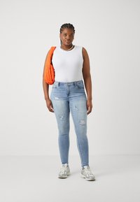 Λευκή αμάνικη μπλούζα, ανοιχτό μπλε σκισμένα skinny τζιν και ασημένια αθλητικά παπούτσια. Πορτοκαλί καπιτονέ τσάντα ώμου και κολιέ από πέρλες ως αξιοσημείωτες λεπτομέρειες.