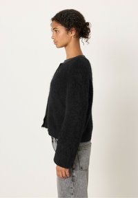 Svart, fluffig cardigan med rund hals, kort design och långa ärmar, bärs över ljusa, högmidjade jeans.