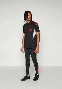 Svart Liverpool FC träningsset bestående av en pikétröja med röda accenter och logo, tillsammans med svarta smala byxor och svarta sportskor.