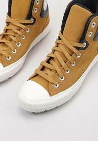 Zapatillas altas de ante en color marrón con acentos en negro, puntera de goma blanca y cordones blancos, con ojales de metal y suela texturizada.