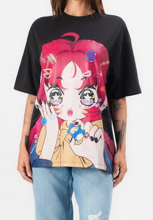 Person trägt ein schwarzes übergroßes T-Shirt mit einem bunten Anime-Stil eines rothaarigen Mädchens, das eine kleine Uhr hält.