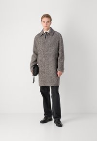 Palton dintr-un amestec de lână gri-maroniu cu un model texturat, închidere cu nasturi și guler larg, asortat cu pantaloni negri și pantofi, purtând o geantă neagră.