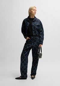 Set in denim, giacca e pantaloni di colore blu scuro con motivo a diamante. Maglione nero sotto. Piccola borsa nera a tracolla, scarpe flat punta.