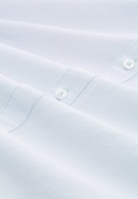 Lichtblauwe katoenen shirt met verticale strepen, voorzien van een knoopsluiting en zichtbare stikdetails op de stof.
