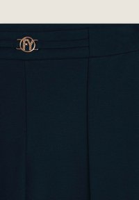 Pantaloni blu navy con texture liscia, caratterizzati da un dettaglio in metallo dorato e pieghe ben ripiegate in vita per un design strutturato.