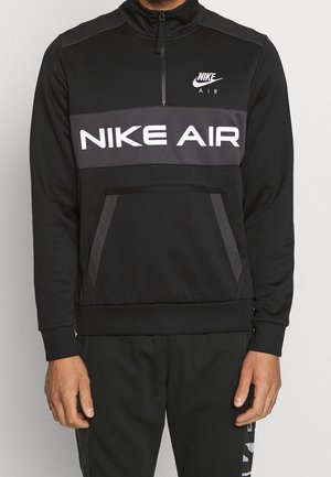 Homme portant un sweat-shirt noir Nike Air avec une fermeture éclair à l'avant, une poche kangourou et des logos blancs Nike Air sur la poitrine et au centre.
