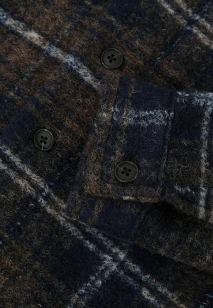 Marineblaue und braune karierten Wollstoff mit strukturierter Oberfläche. Mit schwarzen Knöpfen und einem umgeschlagenen Kragen. Auffällige Fleece-Details.