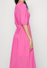 Rosa plissee Kleid mit tailliertem Oberteil, Puffärmeln und cinch-taillierten Mittelteil. Glatte Stofftextur, knielang mit fließender Bewegung.