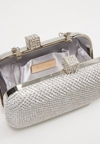 Pochette de soirée en paillettes argentées avec des strass, ouverte pour montrer l'intérieur en satin et le fermoir décoratif avec des strass en forme de cube.