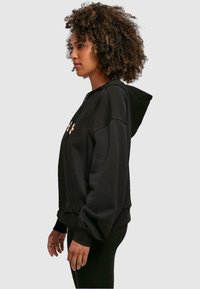 Sudadera con cremallera negra de corte relajado, con capucha, puños acanalados y un diseño floral en el pecho. Textura de tela suave.