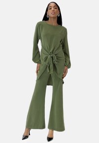 Zweitiliges Outfit in Olivgrün aus weichem Stoff, bestehend aus einem Oberteil mit Knoten vorn und weit geschnittenen Hosen mit lockerem Sitz und langen Ärmeln.