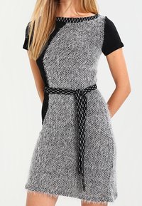 Abito lavorato a maglia in un motivo a spina di pesce nero e grigio, con maniche corte, una silhouette aderente e una cintura decorata in vita.