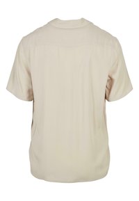 Chemise courte en beige clair à col rond et avec des détails de couture minimaux, présentée de dos sur un fond blanc uni.