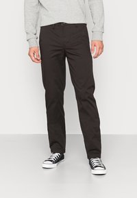 Bruine katoenen broek met een recht model, voorzakken en een knoopsluiting. Gemaakt in combinatie met zwarte canvas sneakers.