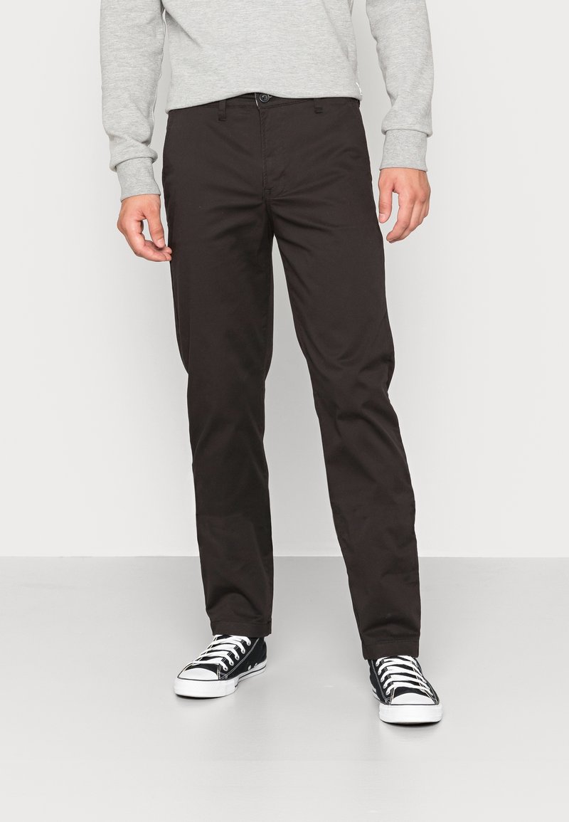Bruine katoenen broek met een recht model, voorzakken en een knoopsluiting. Gemaakt in combinatie met zwarte canvas sneakers.