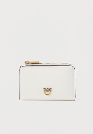 Portefeuille rectangulaire blanc avec une fermeture éclair dorée et un petit emblème doré représentant deux oiseaux se faisant face sur le devant.