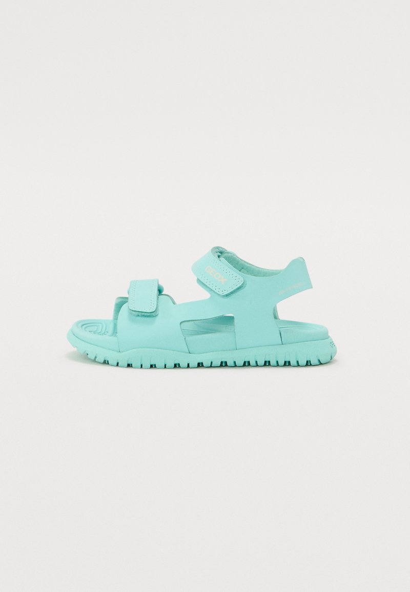 Sandale enfant bleu clair avec brides Velcro réglables et semelle flexible texturée, montrée de profil sur un fond uni.
