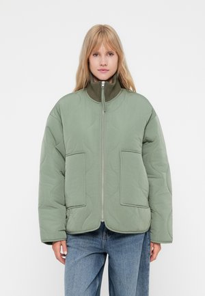 Chaqueta verde acolchada con un alto cuello, cremallera frontal y dos grandes bolsillos. Presenta una textura suave y un diseño de corte holgado.
