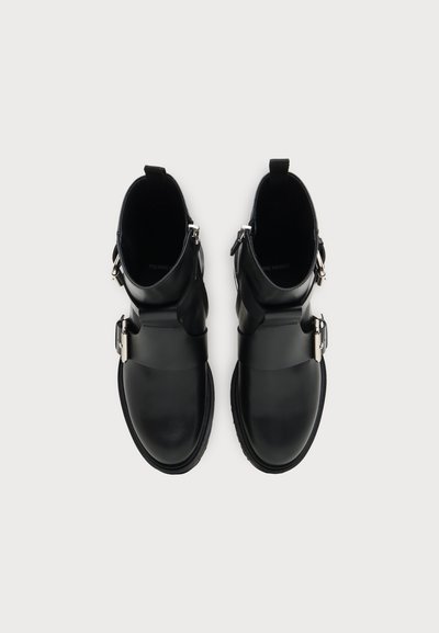 Paire de bottines en cuir noir avec boucles et fermetures éclair argentées, vues de dessus sur fond blanc.