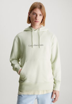 Sudadera verde claro de tela suave, con un bolsillo frontal, puños acanalados y el texto "Calvin Klein Jeans" bordado en el pecho.