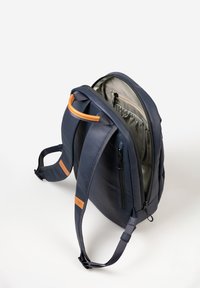 Marineblauer Rucksack aus glattem Material mit braunen Lederakzenten. Verfügt über ein Reißverschlussfach, verstellbare Träger und eine große Öffnung.