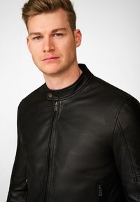 Zwart lederen jack met een staande kraag, ritssluiting aan de voorkant en zijzakken. Gladde textuur met minimale zichtbare stiksels.