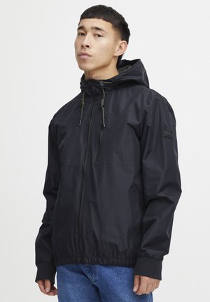 Jachetă neagră tip windbreaker cu glugă, dotată cu fermoar frontal, sireturi ajustabile și manșete elastice. Material neted, rezistent la apă.