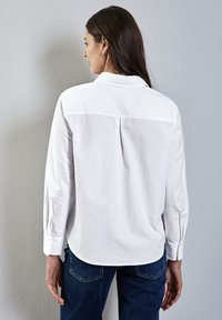 Vit bomullsskjorta med lång ärm, knapp-down krage, ryggveck och sidofickor, i kombination med mörkblå denimjeans.