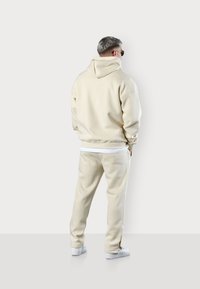 Beige hooded sweatshirt and matching pants, made of soft material. Sweatshirt has a relaxed fit; pants feature side pockets and elastic cuffs.