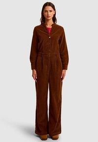 Combinaison en velours côtelé marron avec fermeture boutonnée à l'avant, manches longues et jambes larges. Caractérisée par une taille ceinturée et une texture douce.