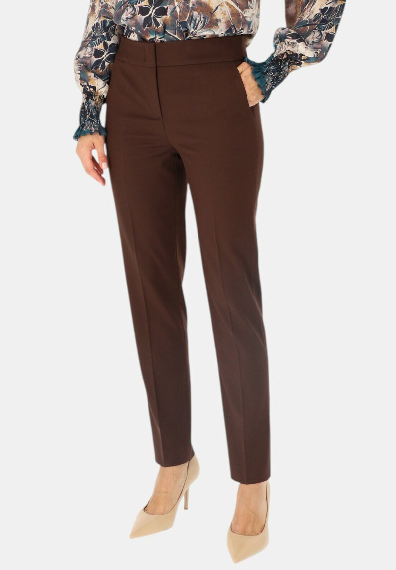 Brązowe dopasowane spodnie o gładkiej fakturze, w wąskim kroju i wysokim stanie. Połączone z beżowymi szpilkami i kwiecistą bluzką.