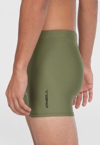 Olivové plavky s úzkym strihom, s hladkým povrchom a čiernym logom "O'Neill" potlačeným na boku.