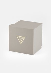Caja gris estriada con un logo dorado triangular y un diseño de signo de interrogación, que presenta líneas limpias y una forma simple y estructurada.