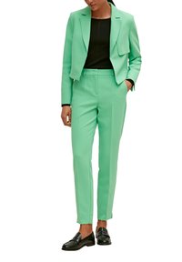 Miętowozielony, dopasowany garnitur z krótką marynarką, pasujące spodnie o prostych nogawkach oraz czarna bluzka. Czółenka w kolorze czarnym dopełniają stylizację.
