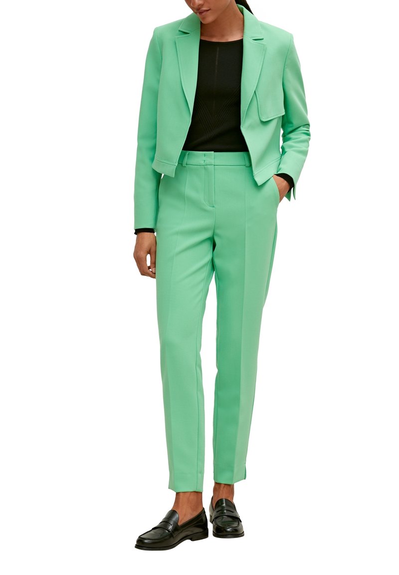 Miętowozielony, dopasowany garnitur z krótką marynarką, pasujące spodnie o prostych nogawkach oraz czarna bluzka. Czółenka w kolorze czarnym dopełniają stylizację.