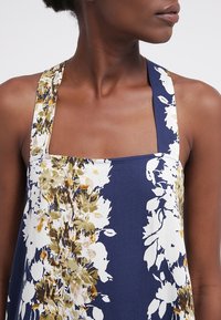 Ärmlös klänning med fyrkantig halsringning, prydd med ett blommönster i gult och vitt på en marinblå bakgrund. Lättviktig tyg, avslappnad passform.