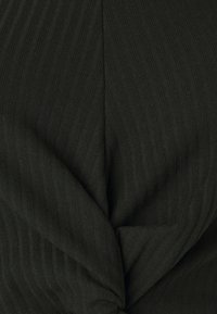 Tejido negro acanalado con un detalle de nudo retorcido; superficie texturizada con rayas verticales que crean una sutil profundidad e interés visual.