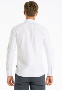 Witte lange mouwen shirt met een knoopsluiting en subtiele textuur, van achter weergegeven, gecombineerd met marineblauwe broek.