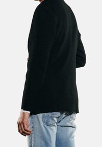 Czarna teksturowana marynarka o dopasowanym kroju, z wyciętym kołnierzem i długimi rękawami, noszona na jasnoniebieskich dżinsach.