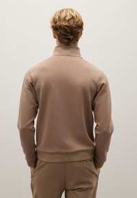 Beige Pullover-Sweatshirt mit weicher Textur, hohem Kragen und gerippten Bündchen. Glattes Design ohne Muster, von hinten betrachtet.