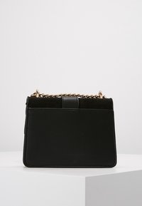 Czarna skórzana torebka o usztywnionym prostokątnym kształcie, z złotym łańcuszkiem oraz zamszowym akcentem na górze.